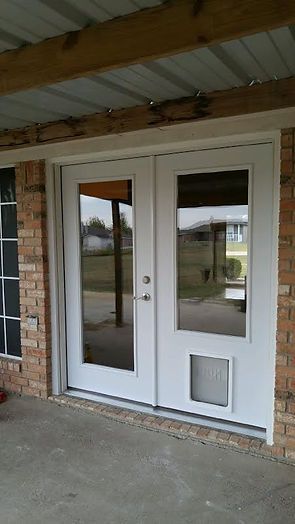 White double doors with glass panels and a dog door, set in a brick building under a covered porch.