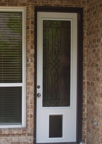 White door with a decorative glass panel and dog door, set in a brick wall, next to a window with blinds.