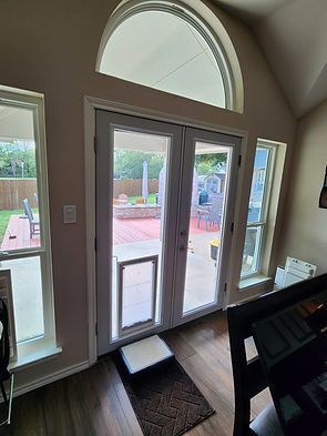 Interior view of French doors with a dog door leading to a patio, flanked by windows.