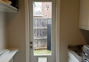 A white door with a window and dog door opens to a backyard with a wooden fence.