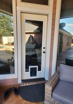 White door with pet door, flanked by windows. Outside seating visible on a patio.