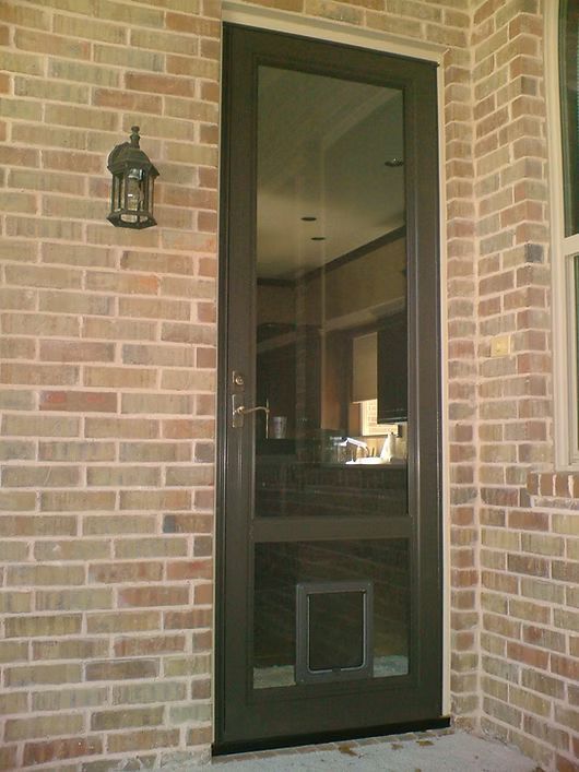 Brown screen door in a brick wall with a small pet door. A black lantern is mounted on the wall.