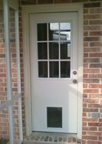 White exterior door with window panes, pet door, set in a brick wall.