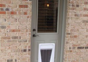 Exterior door with a pet door, set in a brick wall. The door is painted gray, with window and black hardware.