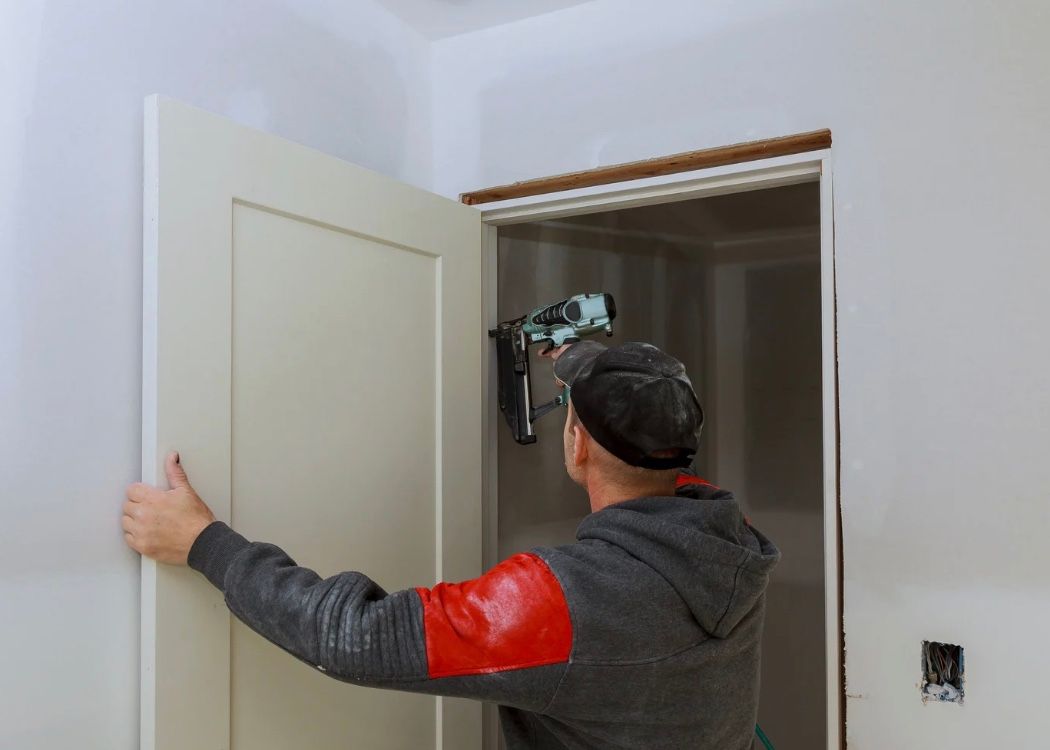 Person installing a door frame with a power tool inside a white room