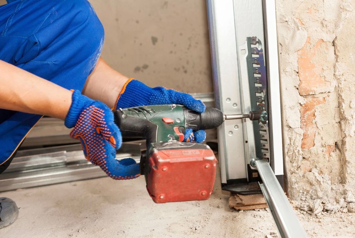 Worker using a handheld drill to cut concrete beside a wall, wearing blue gloves and shirt.