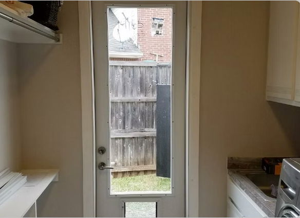 Interior view of a laundry room with a door to a backyard with a wooden fence.