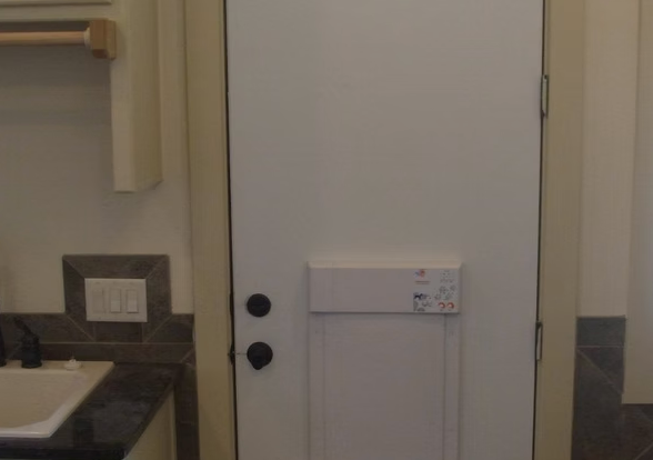 White door with a white security system attached. Black doorknob. Part of a sink and towel rack are visible.
