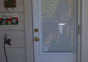 Person reflected in a glass door with a welcome sign and decorative snail on the wall.