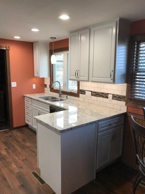 Modern kitchen with white cabinets, dark wood floor, granite island, and orange accent wall.