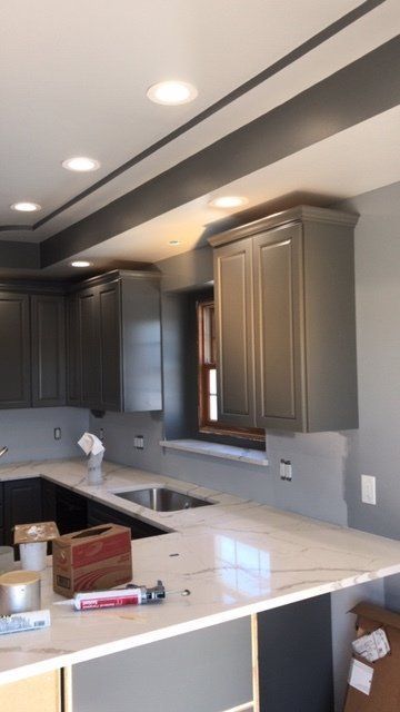 Modern kitchen under renovation with gray cabinets, white countertop, recessed lights, and tools on the island