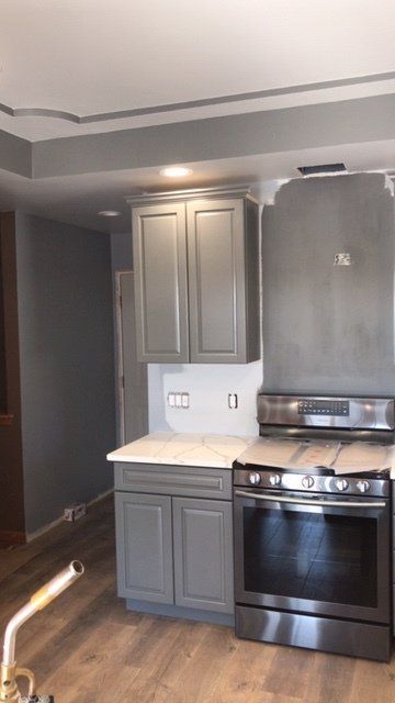 Small modern kitchen with gray cabinets, white countertops, and a stainless steel stove.