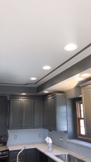 Modern kitchen with dark gray cabinets, recessed ceiling lights, and a window above the counter.