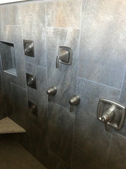Modern tiled shower wall with multiple chrome shower heads and controls