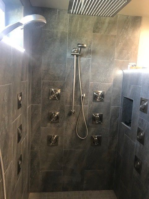 Modern shower with dark tile walls, multiple body jets, and a handheld showerhead