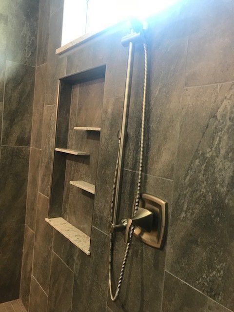 Modern tiled shower with recessed shelves and a handheld showerhead on the right