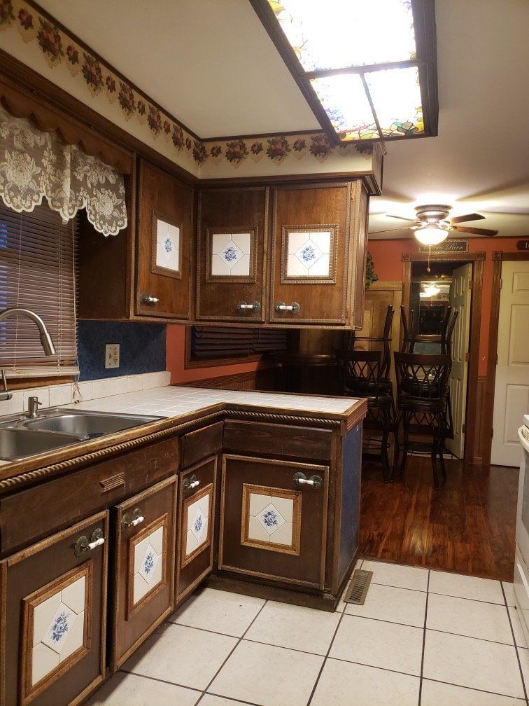 Wood-paneled kitchen with white tile floor, brown cabinets, and a sink under a lace-trimmed window trim