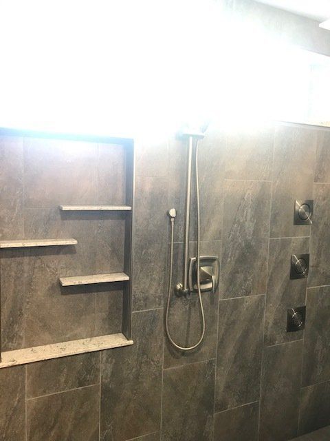 Modern tiled shower with built-in shelves and handheld showerhead under bright light