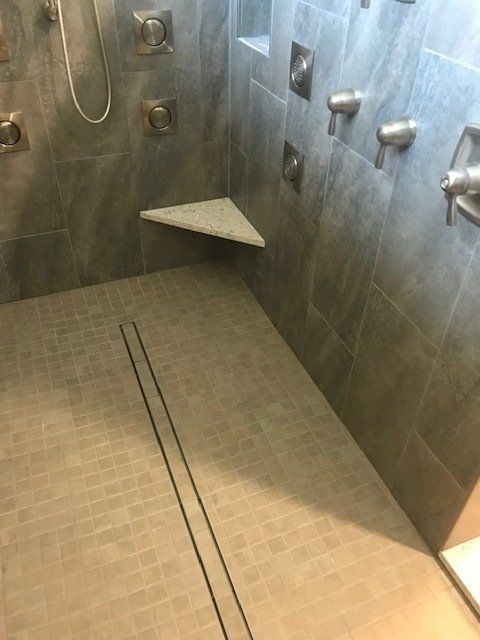 Empty tiled shower with grab bars and a corner shelf, seen from inside.