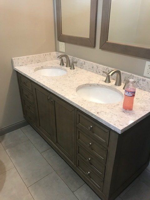 Double sink bathroom vanity with dark cabinets, speckled countertop, mirrors, and a soap bottle on the right.