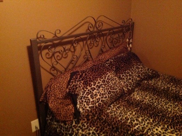 Bed with leopard-print bedding and a decorative metal headboard in a warmly lit room
