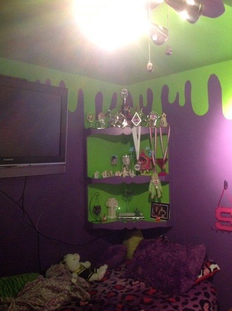 Purple bedroom with green ceiling drips, wall TV, shelf, and a bed with plush toys under bright light