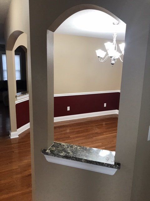 Interior archway opening to a dining room with a chandelier and hardwood floors, plus a small stone ledge.