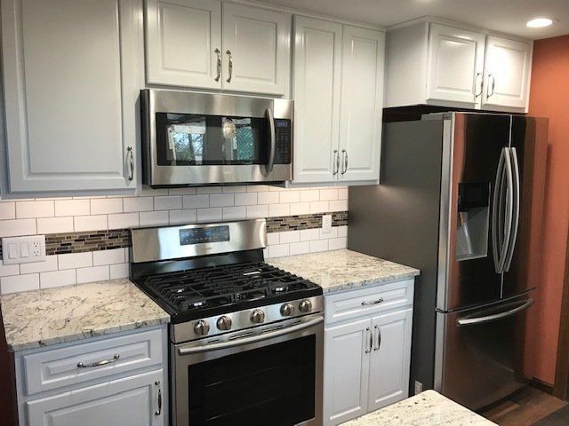 Modern kitchen with white cabinets, stainless steel appliances, and a black stove under a tiled backsplash