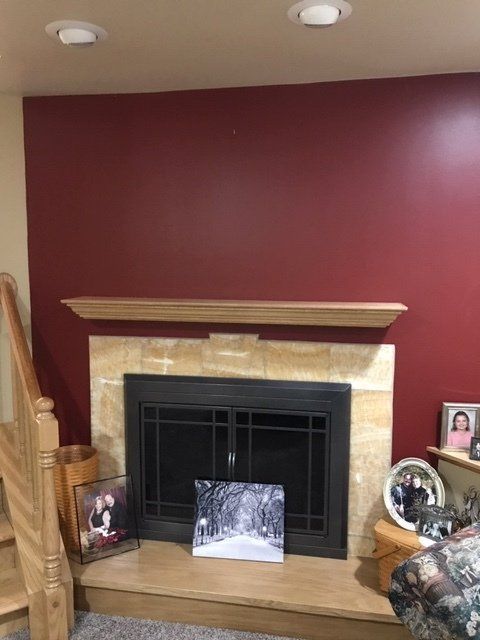 Living room fireplace with beige stone surround, burgundy wall, and framed photos on the mantel and hearth