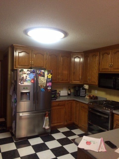 Kitchen with wood cabinets, black-and-white checkered floor, stainless steel fridge, stove, and bright ceiling light