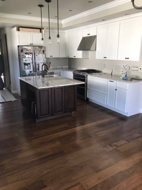 Bright modern kitchen with white cabinets, dark island, stainless appliances, and hardwood floors