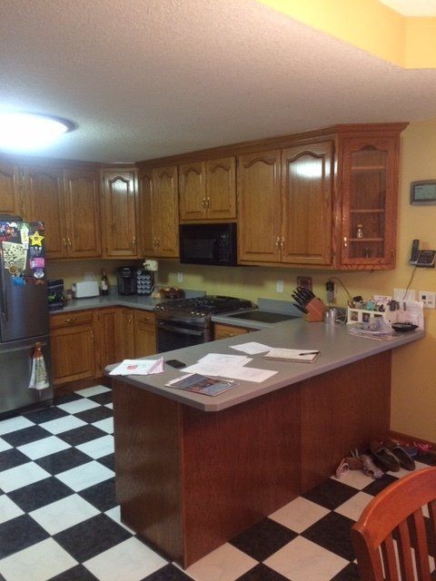 Kitchen with wood cabinets, black-and-white checkered floor, and a large island counter under warm lighting