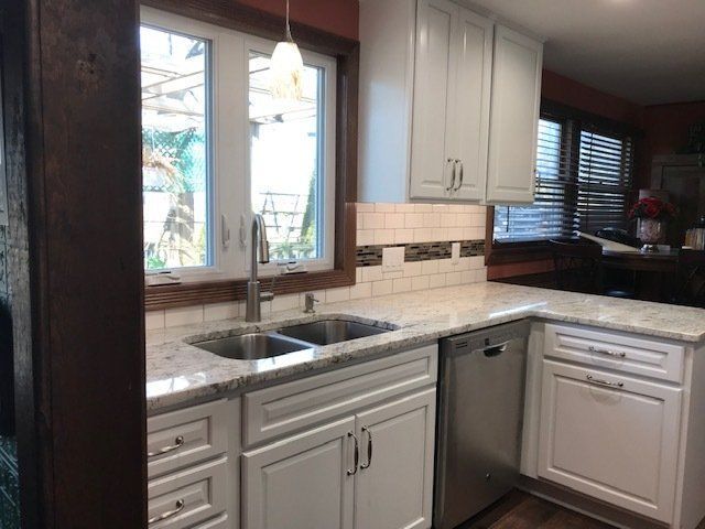 Kitchen countertop with double sink, white cabinets, beige tile backsplash, and a window over the sink