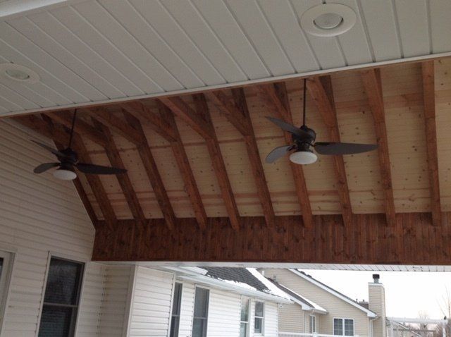 Covered porch ceiling with exposed wooden beams and two ceiling fans above a residential patio.