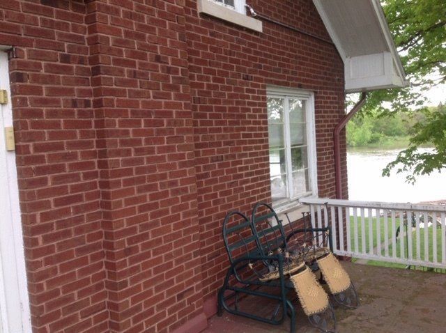 Brick house patio with a metal bench and two beige cushions beside a white door and railing
