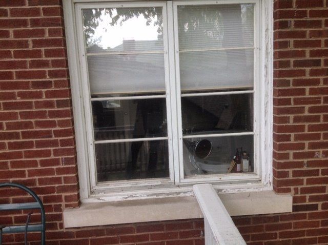Brick wall with a double window and a white downspout leaning into the sill.