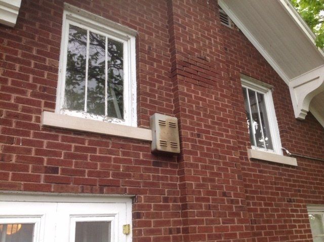 Brick house exterior with two windows and a beige utility meter box on the wall