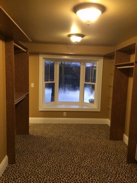 Empty walk-in closet with patterned carpet, wooden shelves, and a window overlooking snow outside.