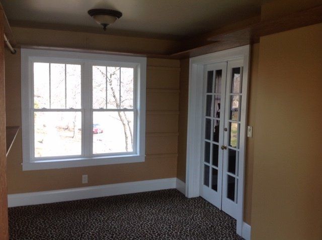 Empty room with tan walls, white trim, large window, and glass French doors on carpeted floor