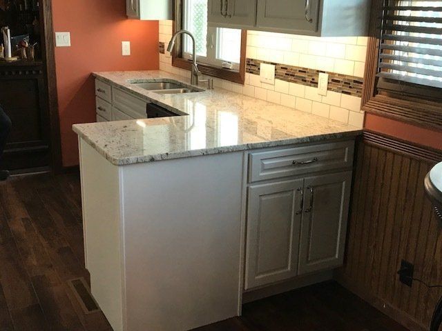 Modern kitchen with granite island, light wood cabinets, and a sink under bright under-cabinet lighting