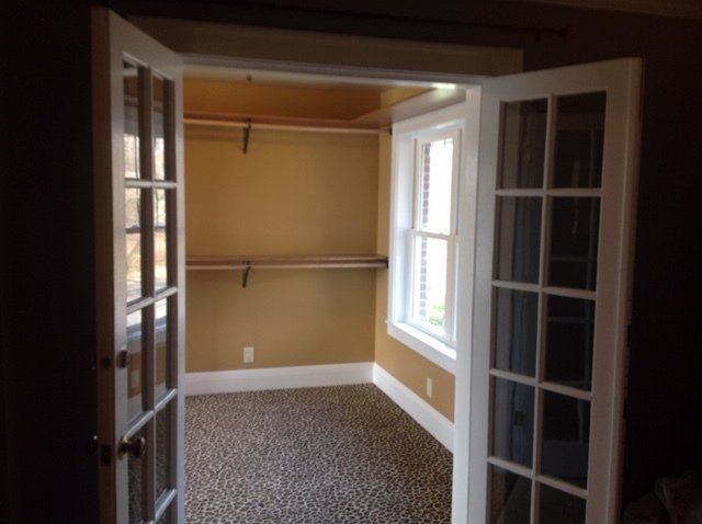 Empty walk-in closet with beige walls, white shelves, and dark French doors