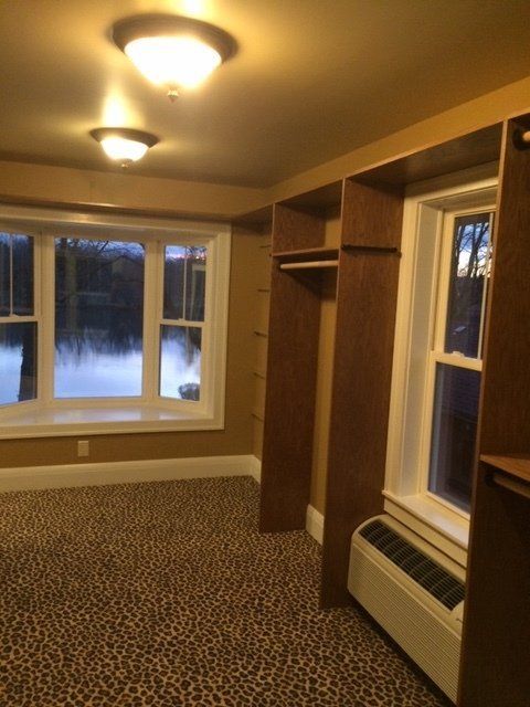 Empty room with carpet, beige walls, ceiling lights, and windows showing snow outside