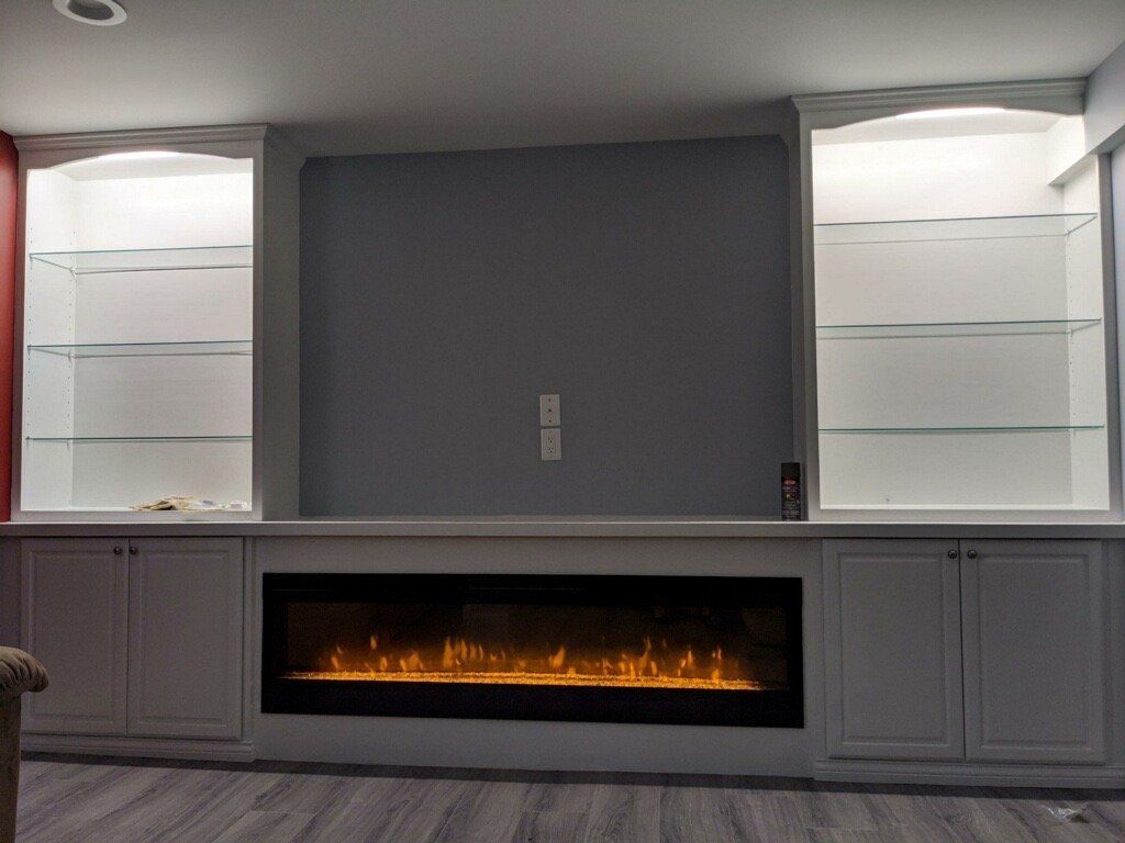 Built-in fireplace with dark gray wall, white cabinets, and lit electric fire beneath glass shelves