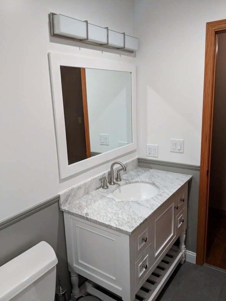 Modern bathroom vanity with white sink, mirror, gray walls, and wood door