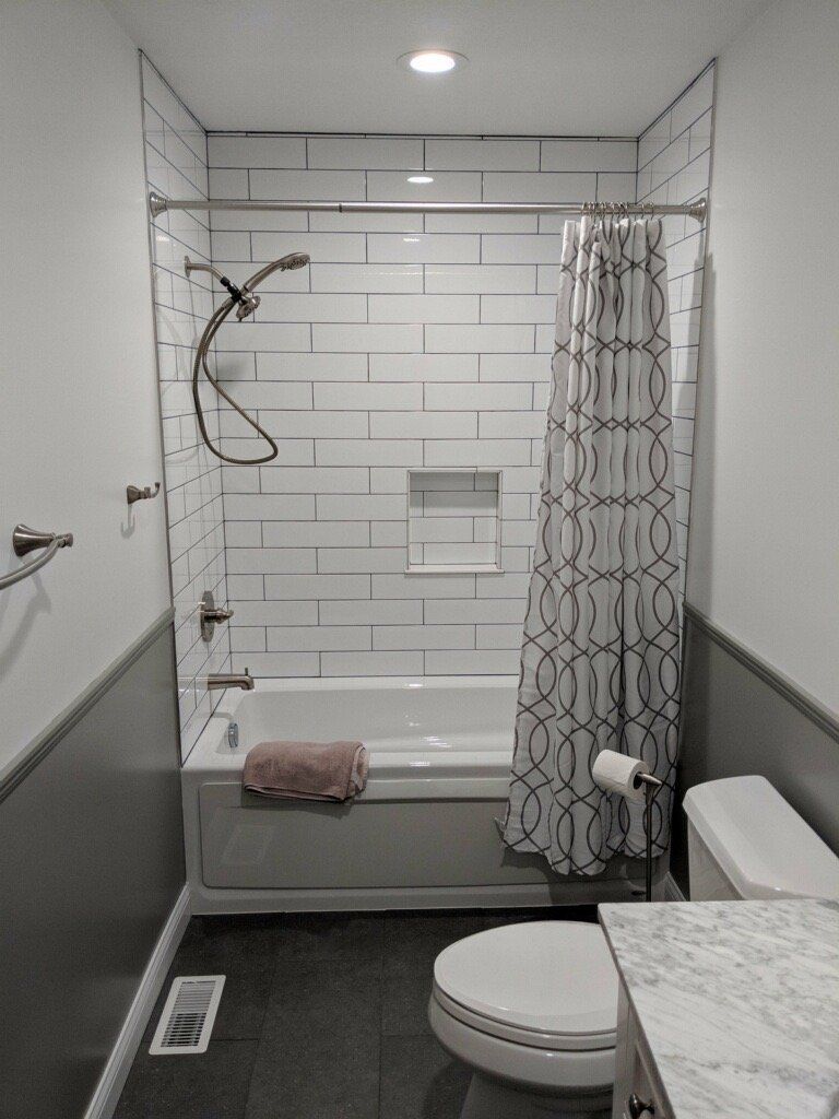 Small bathroom with shower, toilet, vanity, and white tile walls.