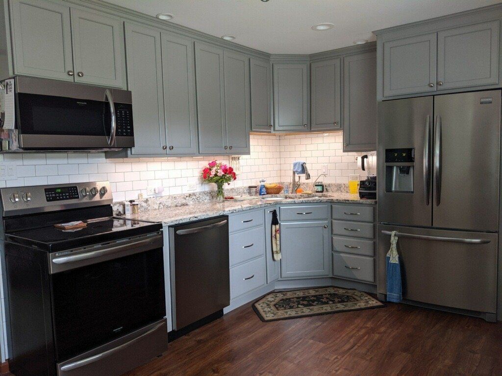 Modern kitchen with gray cabinets, black appliances, stainless fridge, and light countertops