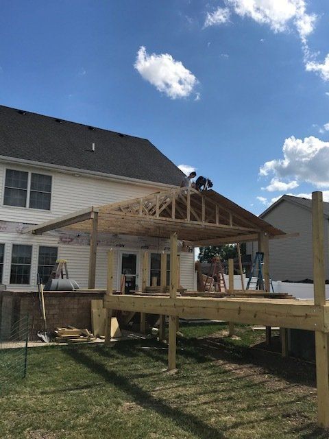 Workers framing a wooden backyard deck addition beside a white house under a blue sky