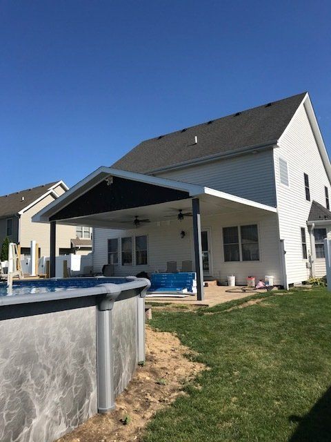 Backyard with an above-ground pool beside a covered patio and a white house on a sunny day