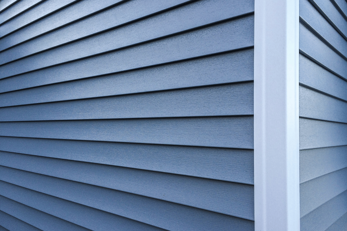 Blue vinyl house siding meeting at a white corner trim.