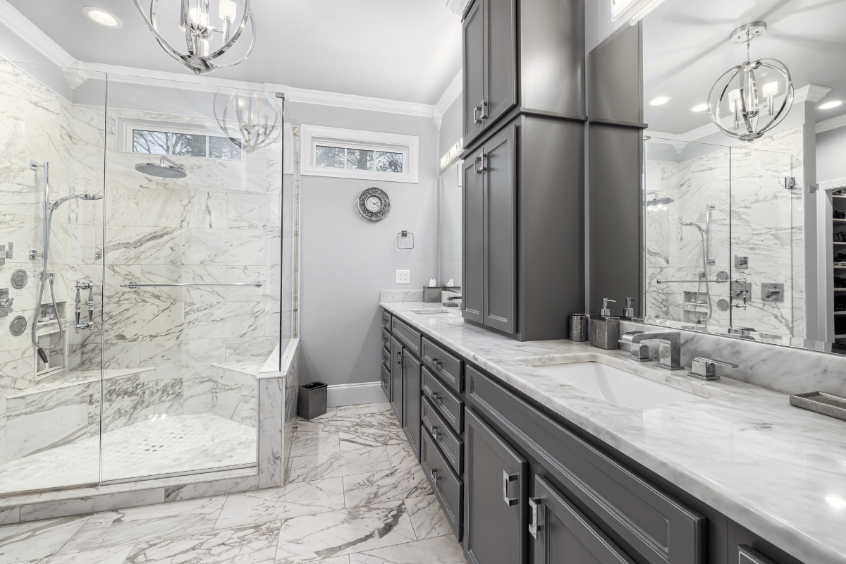 Luxurious marble bathroom with glass shower, double vanity, and gray cabinetry